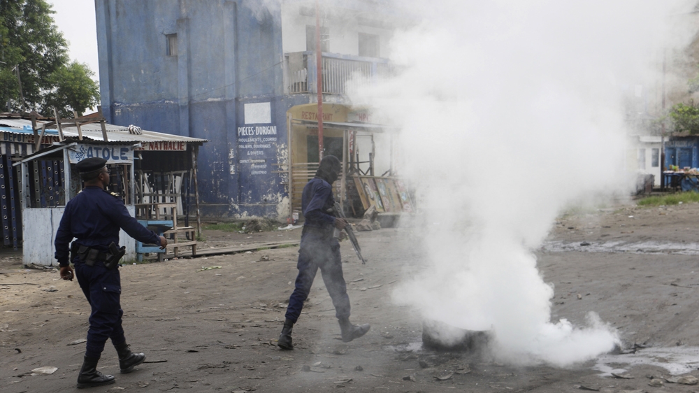 Policemen walk past burning debris during protests in Kinshasa on Sunday [John Bompengo/AP]