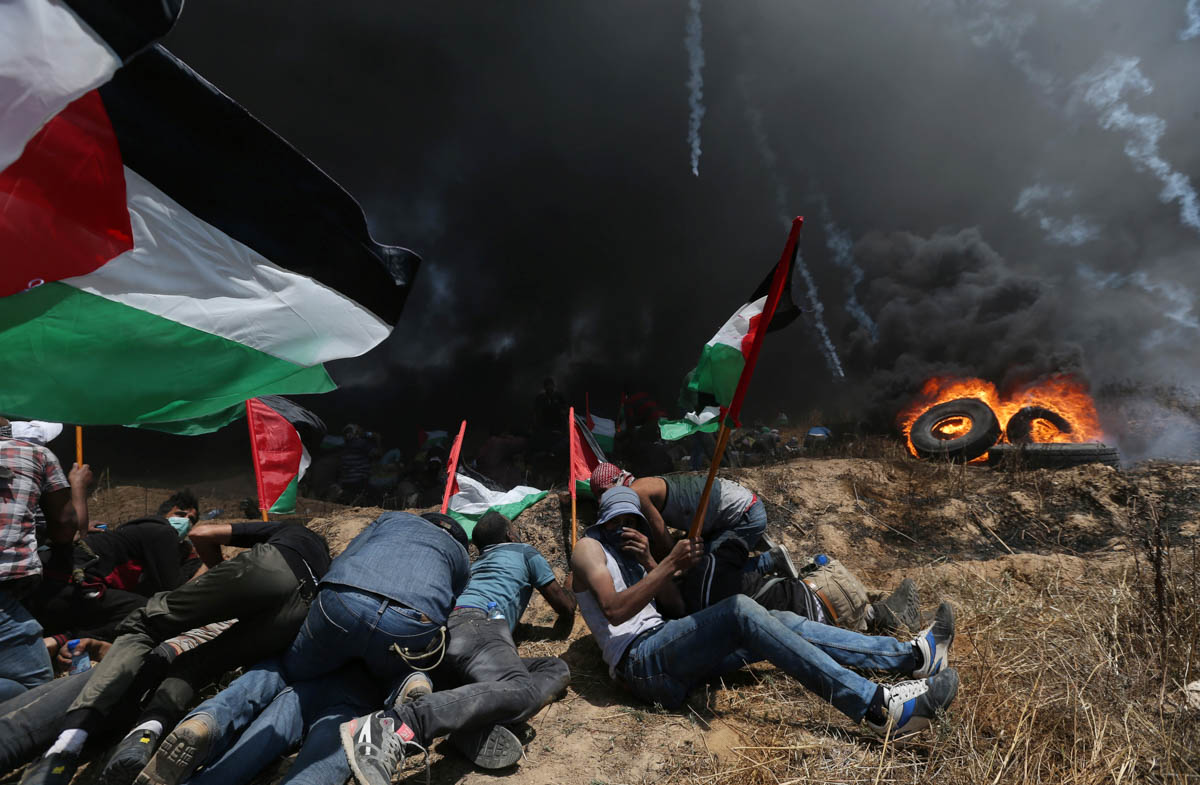 Palestinian demonstrators take cover from Israeli fire and tear gas during a protest against U.S. embassy move to Jerusalem and ahead of the 70th anniversary of Nakba, at the Israel-Gaza border in the