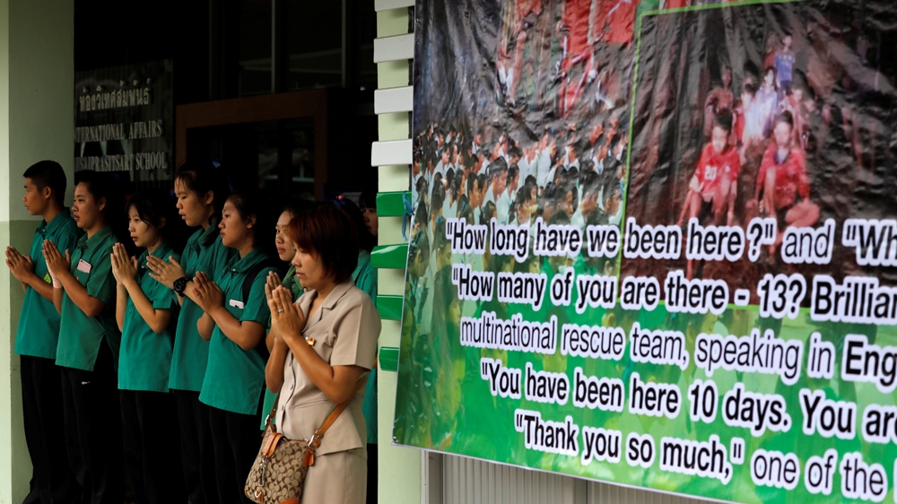 Schoolmates pray next to a banner showing the team who were trapped at Mae Sai Prasitsart school on Monday morning [Tyrone Siu/Reuters]