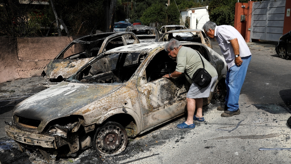 People look inside a burned-out car following a wildfire at the village of Mati [Alkis Konstantinidis/Reuters]