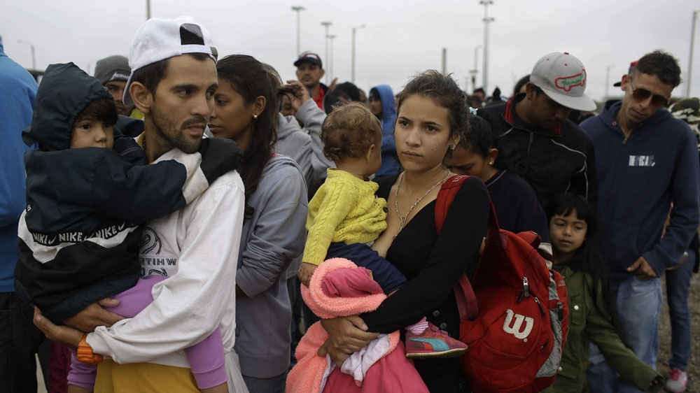 Jorge Gonzales and his wife Kenia, carrying their boys, wait in line for breakfast, after crossing the border into Peru [Martin Mejia/AP Photo]
