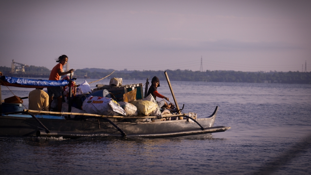 A bangka, or small wooden outrigger boat, cuts across Masinloc Bay, piled high with scrap metals and other recyclable items collected from the islands. These will likely be sold in the mainland for spare change. [Santiago Arnaiz/Al Jazeera]