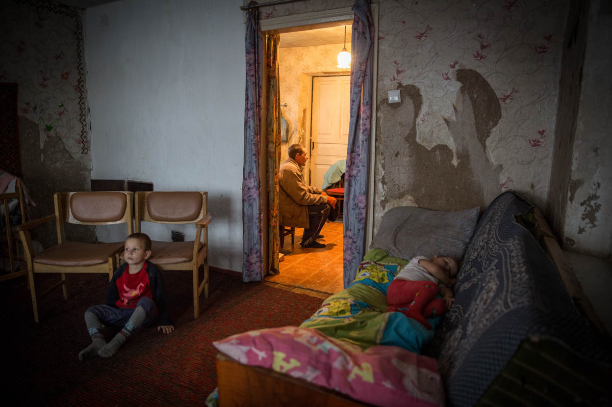 Iliya, 5, is watching TV while his father Viktor has a short rest in the kitchen. The youngest girl Aryna, 2, is having her afternoon nap. Their house was heavily damaged during the early days of war,