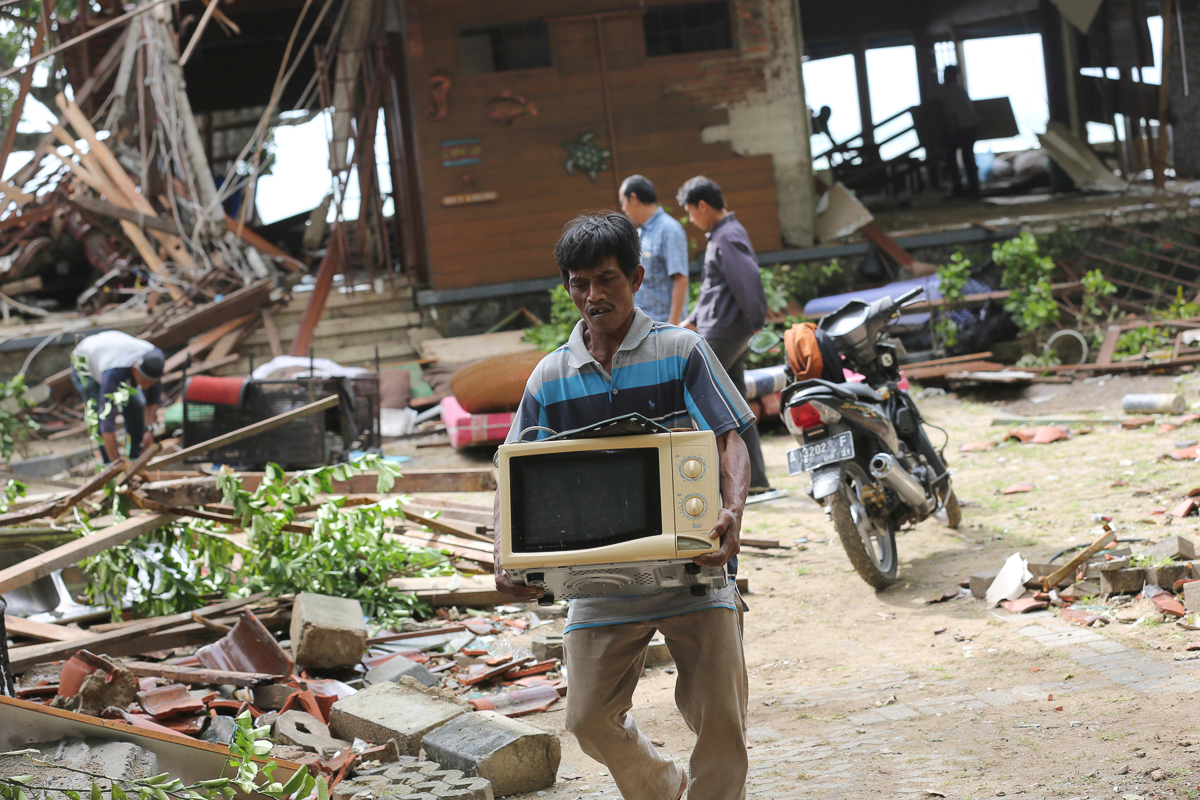 A man carries a usable item following a tsunami in Carita beach, Indonesia, Monday, Dec. 24, 2018. Doctors worked to save injured victims while hundreds of military and volunteers scoured debris-strew