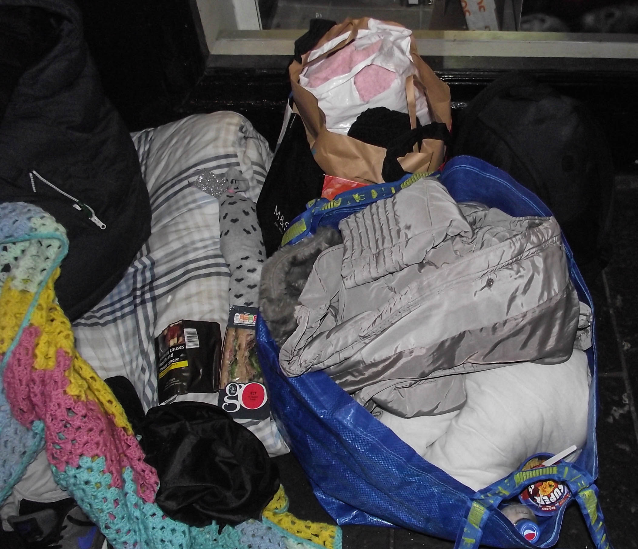 These items, which belong to Sally*, include a sleeping bag, blankets, a sandwich she has been given and a packet of instant noodles [Alasdair Soussi/Al Jazeera]