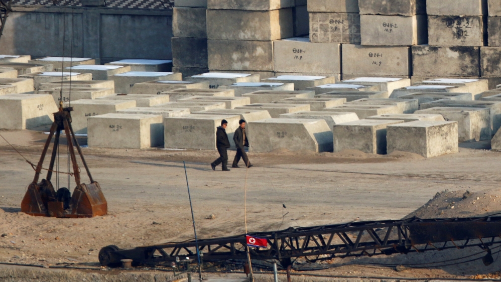 Men walk past concrete piers near a North Korean flag at a shipyard in Sinuiju