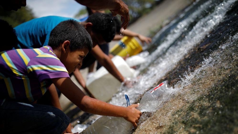 People collect water released through a sewage drain that feeds into the Guaire River in Caracas [Carlos Garcia Rawlins/Reuters]
