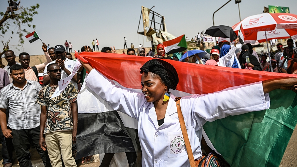 A Sudanese woman walks with a national flag spread behind her as people continue to protest outside the army complex in the capital Khartoum on April 17, 2019. - Sudanese protesters hardened their dem
