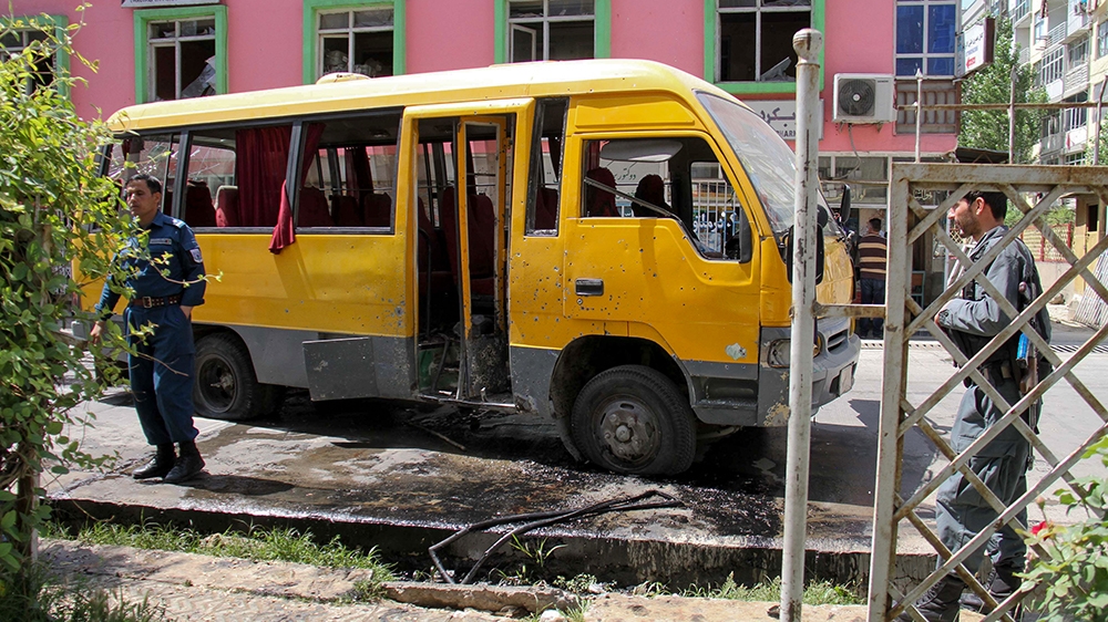 Afghan security personnel stand near the a damage bus carrying university students at the site of the successive bomb blasts in Kabul on June 2, 2019. - One person was killed and at least 17 others wo