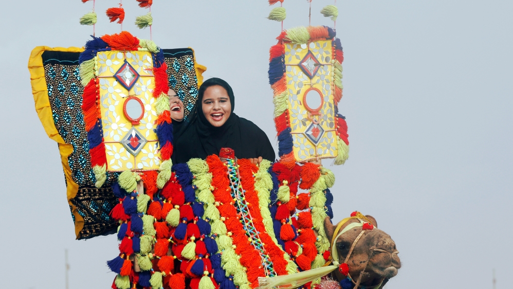 Women react as they ride a camel during Eid al-Fitr celebrations, at Clifton beach in Karachi