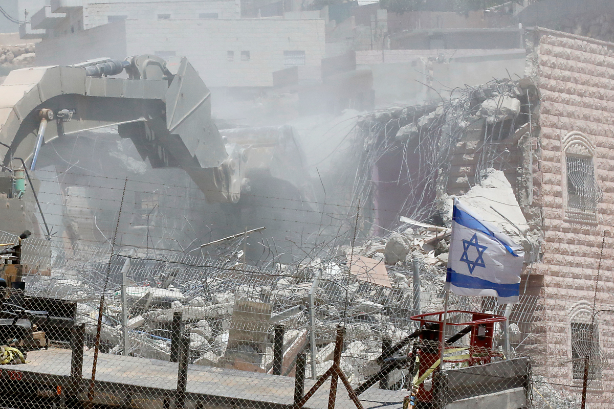 This picture taken from the West Bank on July 22, 2019 shows an Israeli flag waving as Israeli security forces tear down one of the Palestinian buildings still under construction which have been issue