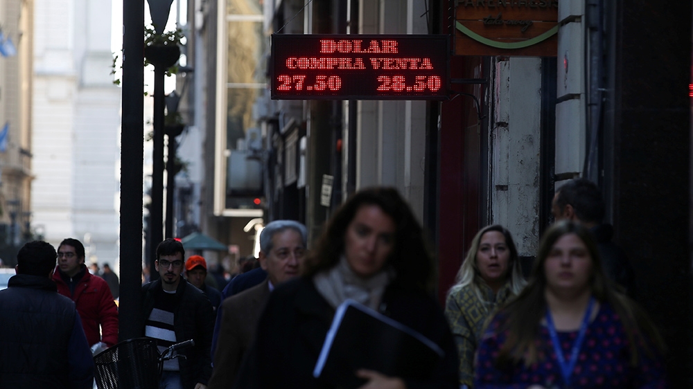 Pedestrians walk past an electronic board showing currency exchange rates in Buenos Aires'' financial district, Argentina