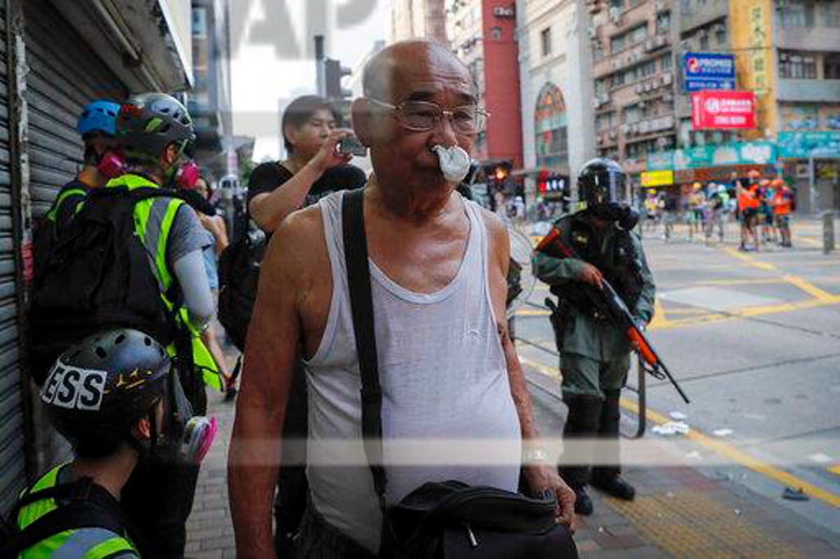 A man reacts from tear gas as protesters face off with riot policemen on a street in Hong Kong, Sunday, Aug. 11, 2019. Police fired tear gas late Sunday afternoon to try to disperse a demonstration in