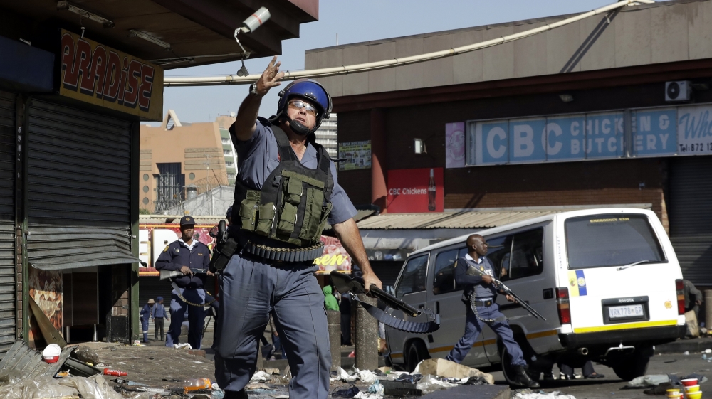 A riot police officer throws a teargas canister as looters make off with goods from a store in Germiston, east of Johannesburg, South Africa, Tuesday, Sept. 3, 2019