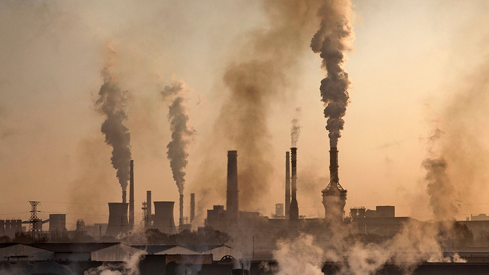INNER MONGOLIA, CHINA - NOVEMBER 04: Smoke billows from a large steel plant as a Chinese labourer works at an unauthorized steel factory, foreground, on November 4, 2016 in Inner Mongolia, China. To m