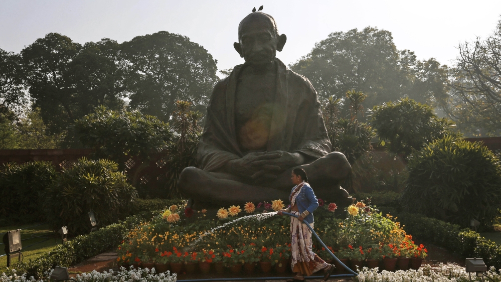 A worker waters plants around a statue of Mahatma Gandhi inside the premises of Parliament as Indian Finance Minister Palaniappan Chidambaram delivers the annual budget in New Delhi, India, Thursday,