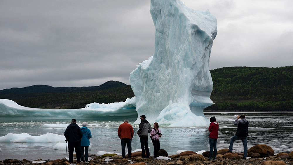(FILES) In this file photo taken on July 3, 2019, tourists look at an iceberg from the seashore of King''s Point in Newfoundland, Canada. - The world must slash its emissions of planet-warming greenhou