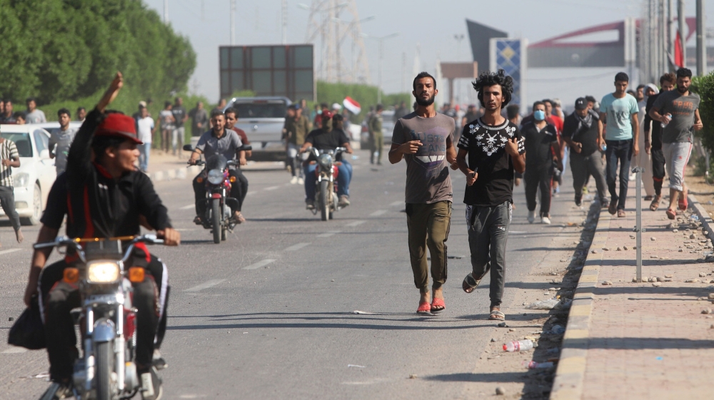 Iraqi demonstrators run away during clashes with Iraqi army forces, guard at the entrance of Umm Qasr Port during ongoing anti-government protests, south of Basra