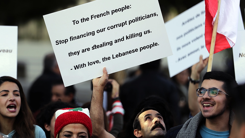 Lebanese anti-government demonstrators hold placards outside the French embassy in the capital Beirut on December 11, 2019
