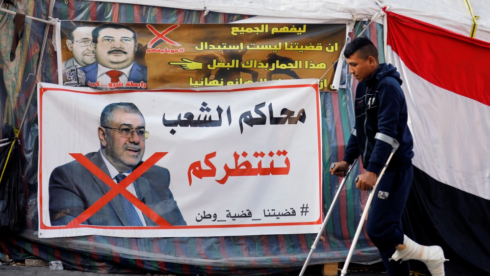 An Iraqi demonstrator on crutches walks next to a poster depicting the outgoing Higher Education Minister Qusay al-Suhail, nominee for the prime minister office in Iraq, during ongoing anti-government