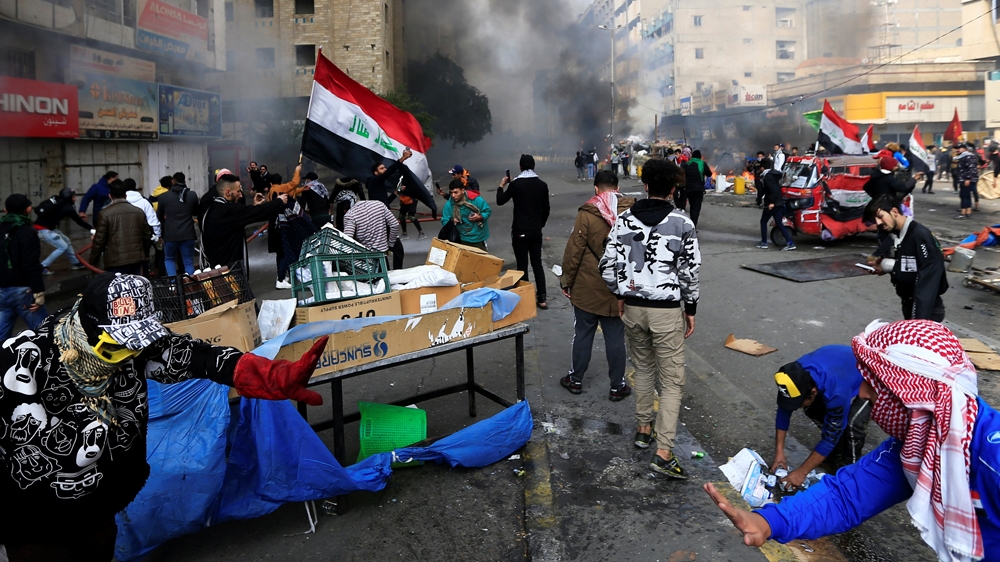 Demonstratos are seen amongst smoke rising from burning tents as Iraqi security forces raid at Tahrir Square during ongoing anti-government protests in Baghdad