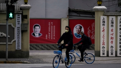 People wearing masks pass by portraits of Chinese President Xi Jinping and late Chinese chairman Mao Zedong as the country is hit by an outbreak of the novel coronavirus, on a street in Shanghai