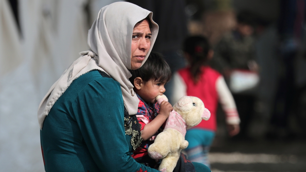 An internally displaced child carries a stuffed animal as he sits on a woman''s lap at a makeshift camp in Afrin