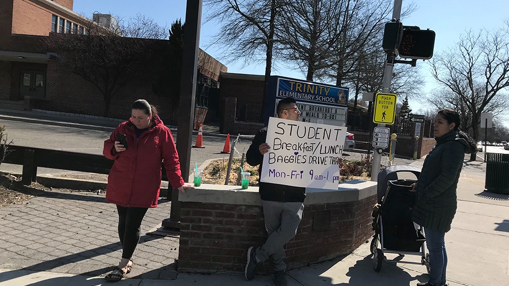 Mario Bravo, a school safety aide at New York’s Trinity Elementary School, holds a sign about free bagged meals for schoolchildren, while schools are closed due to the coronavirus disease (COVID-19) outbreak