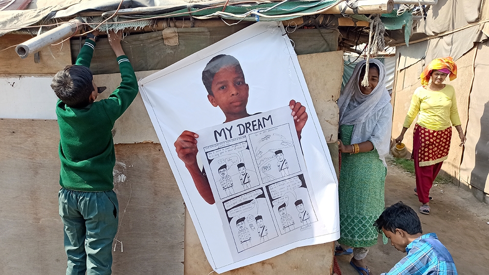 Asmat Ullat, 12, putting helping to put up a poster of his comic “My Dream” [Tasnim Nazeer/Al Jazeera]