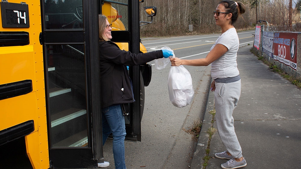 Christine Twiss delivers sack lunches to Marsha Spencer on a school bus route converted to a meal delivery route for the Marysville School District, as schools close during the coronavirus disease (COVID-19) outbreak, on the Tulalip Indian Reservation in Tulalip, Washington