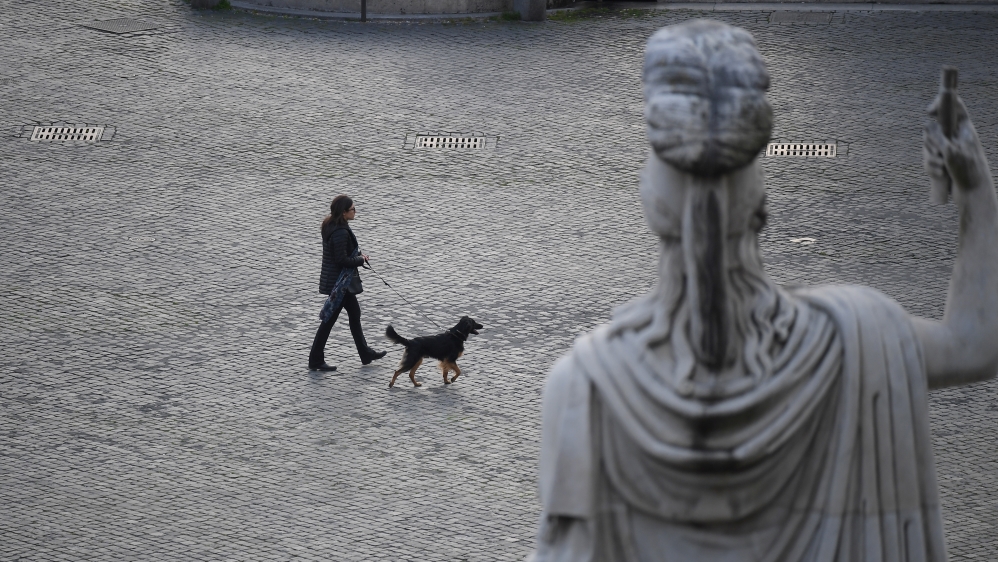 A woman with her dog is seen crossing the deserted Piazza del Popolo while the Italians stay at home as part of a lockdown against the spread of coronavirus (COVID-19) in Rome