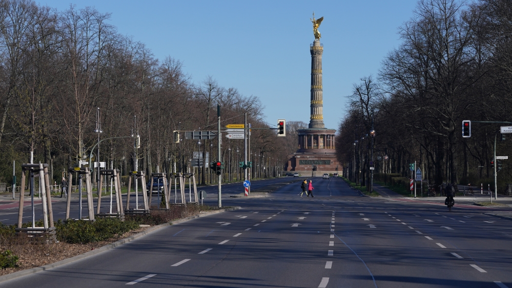 People cross a nearly-empty street leading to the Victory Column at Tiergarten park in the city centre in Berlin, Germany