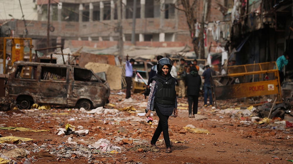 In this Thursday, Feb. 27, 2020, a television reporter holds a microphone as she walks through a street vandalized in Tuesday's violence in New Delhi, India. Reporting in India has never been without 