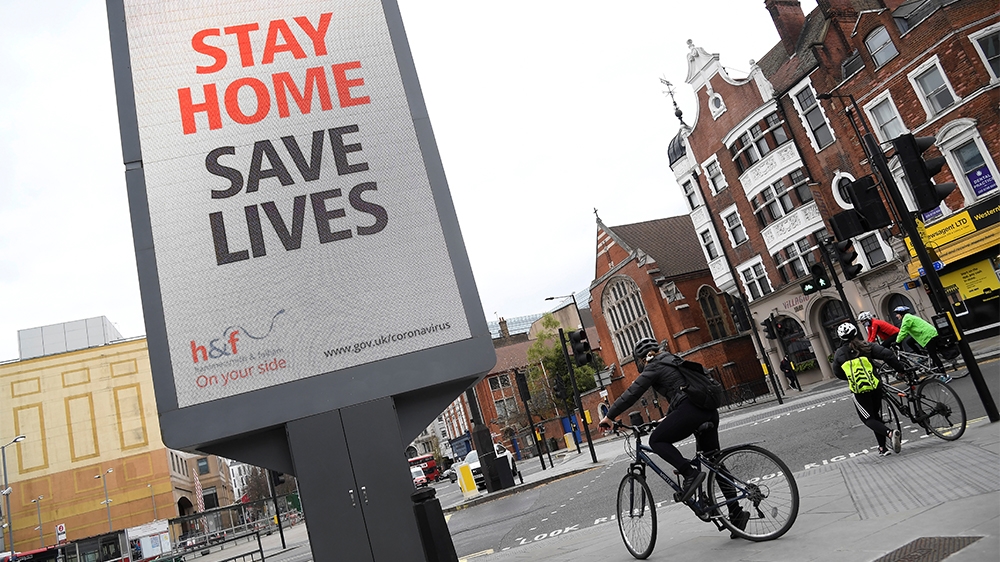 Cyclists pass an electronic billboard displaying a Public health information campaign message from the UK government and local government in London as the spread of the coronavirus disease (COVID-19)