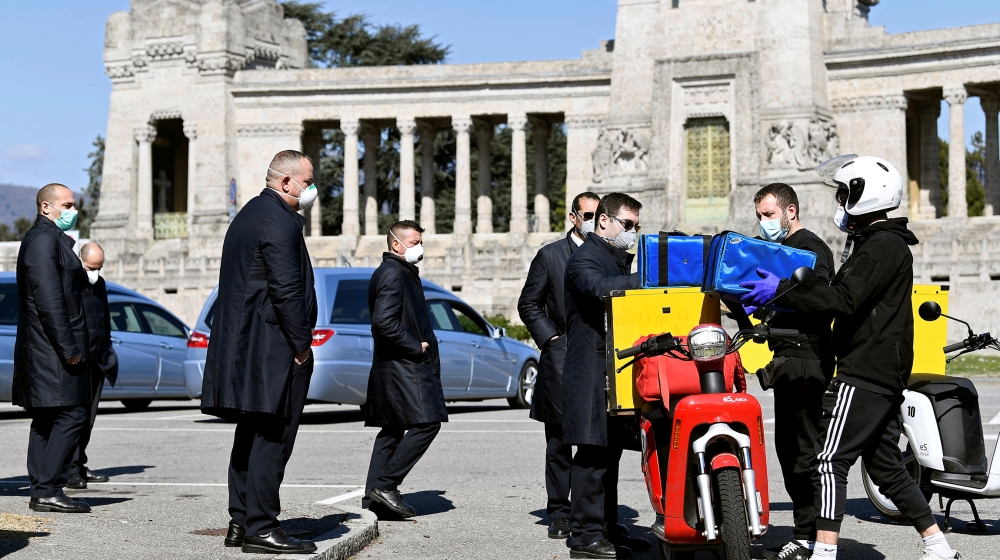 Drivers of hearses wearing protective face masks, receive a pizza delivery as they wait outside a cemetery to collect coffins of those who have died from coronavirus disease (COVID-19) in Bergamo, Ita