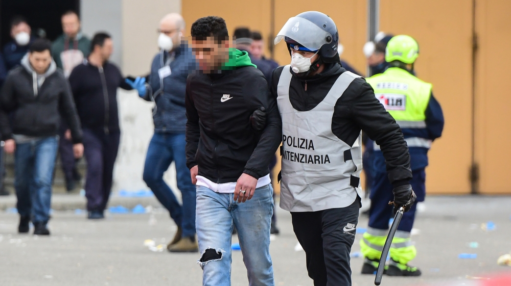 A prison guard wearing a respiratory mask (R) escorts an inmate across a yard of the Sant'Anna prison in Modena, Emilia-Romagna, as some inmates are transfered from a building to another, in one of It