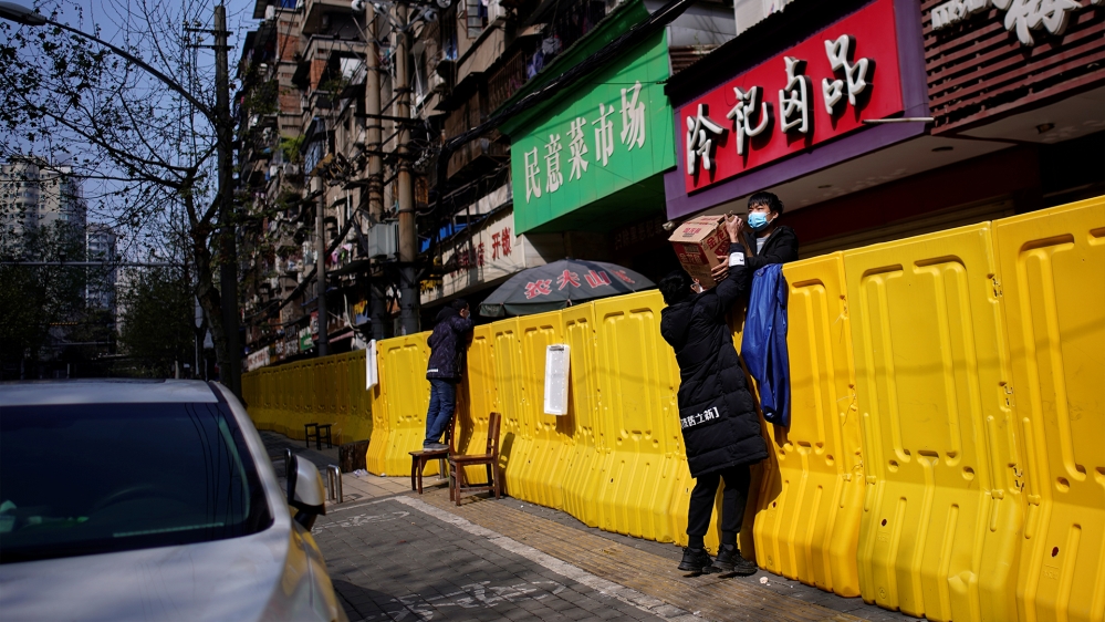 Residents pay for groceries over barriers set up to ring fence a wet market on a street in Wuhan