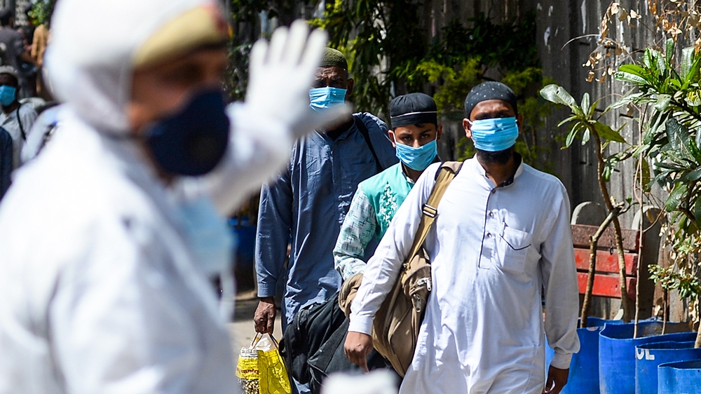 A policeman (L) gestures as men wearing protective facemasks walk to board a special service bus taking them to a quarantine facility amid concerns about the spread of the COVID-19 coronavirus in Niza