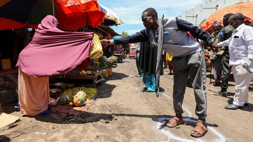 A Somali woman sells fruits to a customer standing at a social distancing signage, as a measure to stem the growing spread of the coronavirus disease (COVID-19) outbreak, at the market centre in Hamar