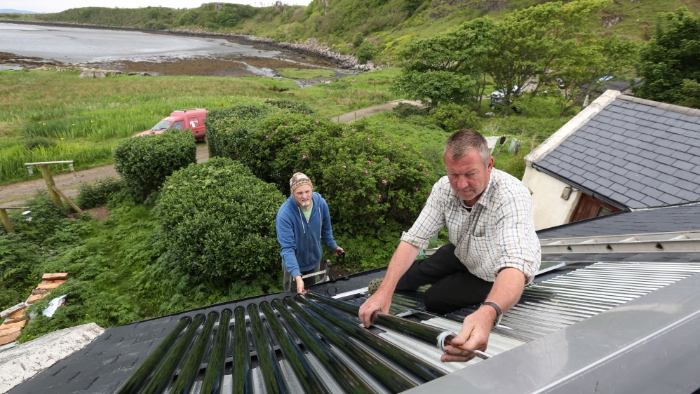Brian Gardner and Ben Cormack fit solar thermal water heaters onto the roof of a cottage on the island of Eigg, Inner Hebrides, Scotland