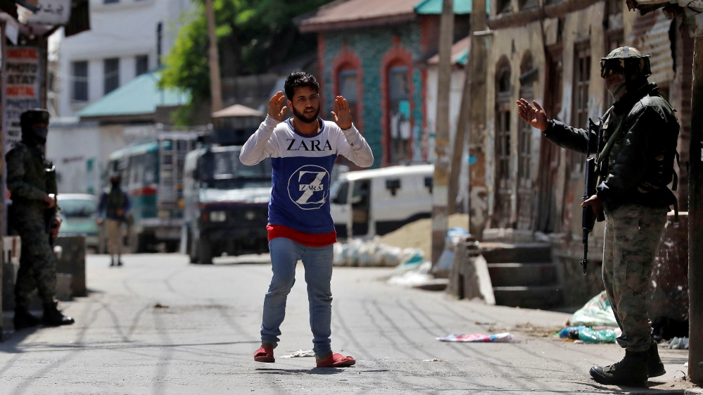 A civilian raises his hands as he moves past Indian soldier in Kashmir