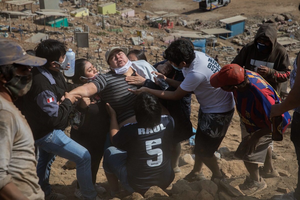 Relatives comfort a family member during the burial service of 85-year-old Lupicino Fernandez, who died of the new coronavirus, at the Nueva Esperanza cemetery on the outskirts of Lima, Peru, Wednesda