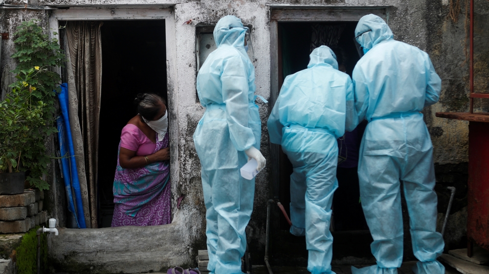 A woman watches as healthcare workers check the temperature of residents of a slum, in Mumbai