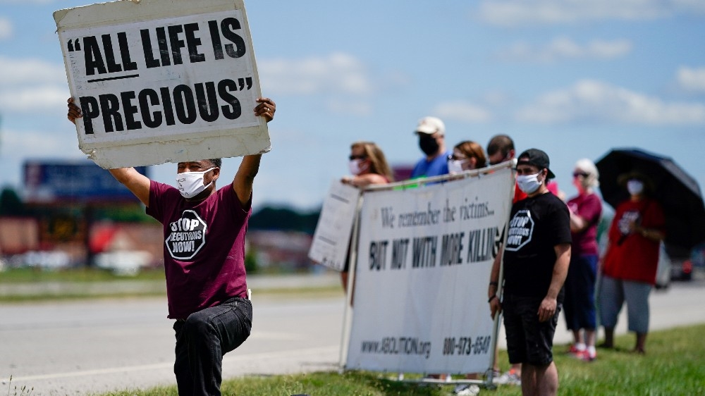 Reverend Sylvester Edwards kneels as other protesters hold signs near a Federal Correctional Complex to show their opposition to the death penalty and the execution of Daniel Lewis Lee [Reuters]