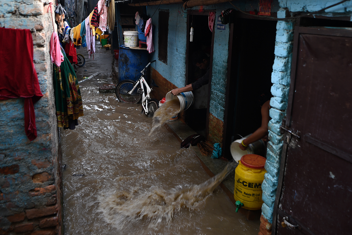 Residents use buckets to remove water entering in their house after the Bagmati River overflowed following monsoon rains in Kathmandu on July 20, 2020. - The death toll from heavy monsoon rains across