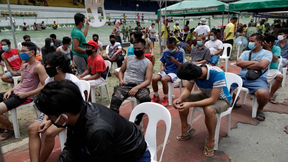 Men who got arrested for violating quarantine health protocols await for police instruction inside a stadium in Manila
