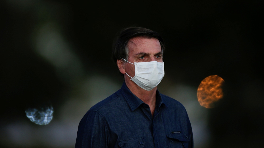 Brazil’s President Jair Bolsonaro observes a ceremony to lower the Brazilian flag for the night at the Alvorada Palace as he continues to battle the coronavirus
