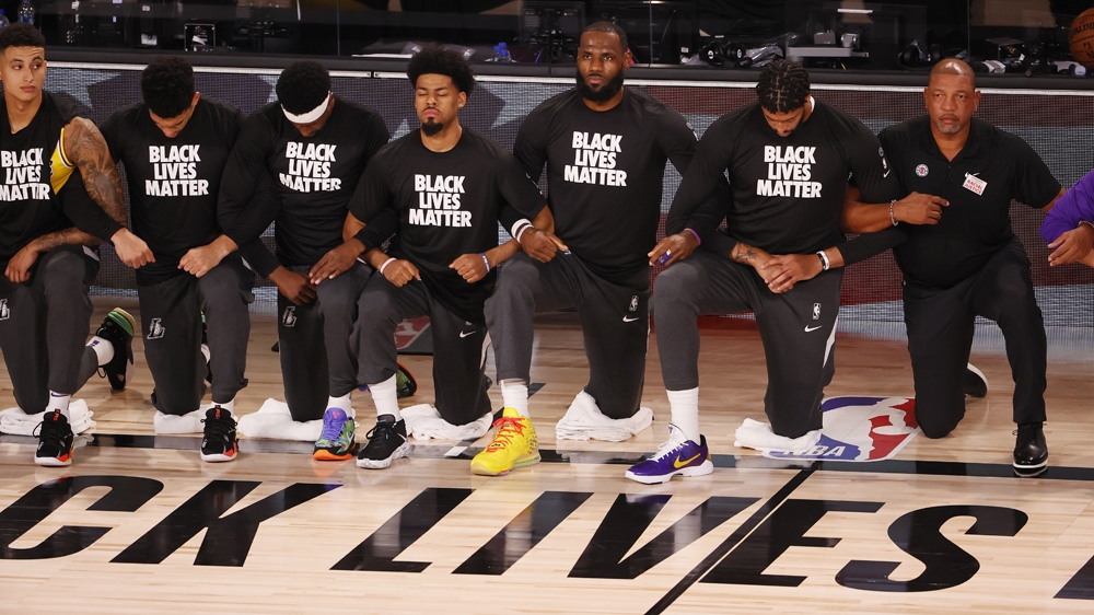 Basketball players and coaches from the Los Angeles Lakers and the Los Angeles Clippers locking arms and taking a knee during the national anthem before their game restarting the NBA season in Kissimmee, Florida, US