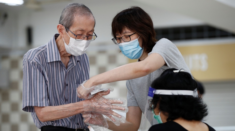 A relative helps a voter put on plastic gloves, as part of preventive measures against COVID-19 at a Singapore polling station