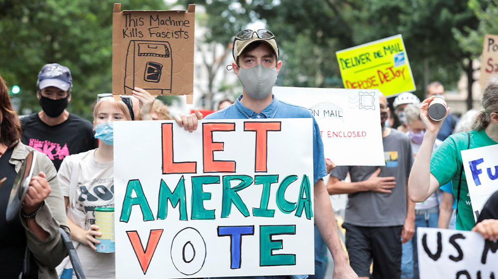 Demonstrators march to the condo of Postmaster General Louis DeJoy to protest against changes in the postal service in Washington, DC